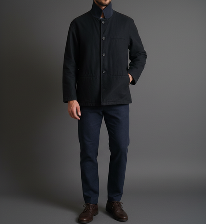 Man wearing a dark coat and jeans against a gray background